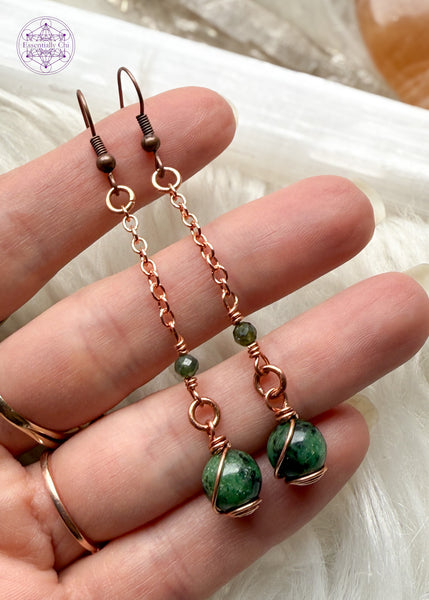 Gorgeous deep green Ruby Zoisite dangle earrings hang from a long copper chain and swirled in copper wire with green tourmaline faceted accent bead. Hung on brass ear hooks gives them a total length of 2.75". Held in hand to show size reference.