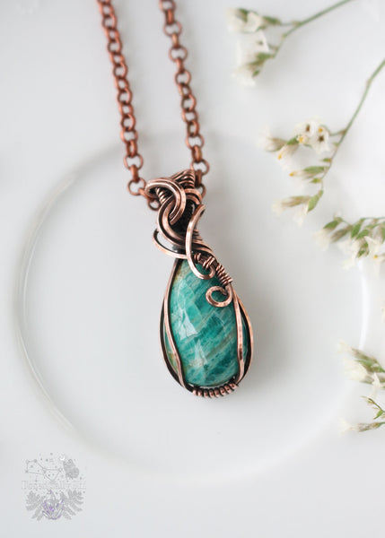 Experience the gentle embrace of our Eleos Dainty Amazonite Copper Wire Wrapped Pendant. Named after the goddess of mercy, this piece features a Russian Amazonite crystal in a beautiful copper wire-wrapped design, promoting emotional healing and compassion for empaths. The bail design wraps around itself like a little hug, which is what I feel Amazonite is good for being a heart chakra crystal.