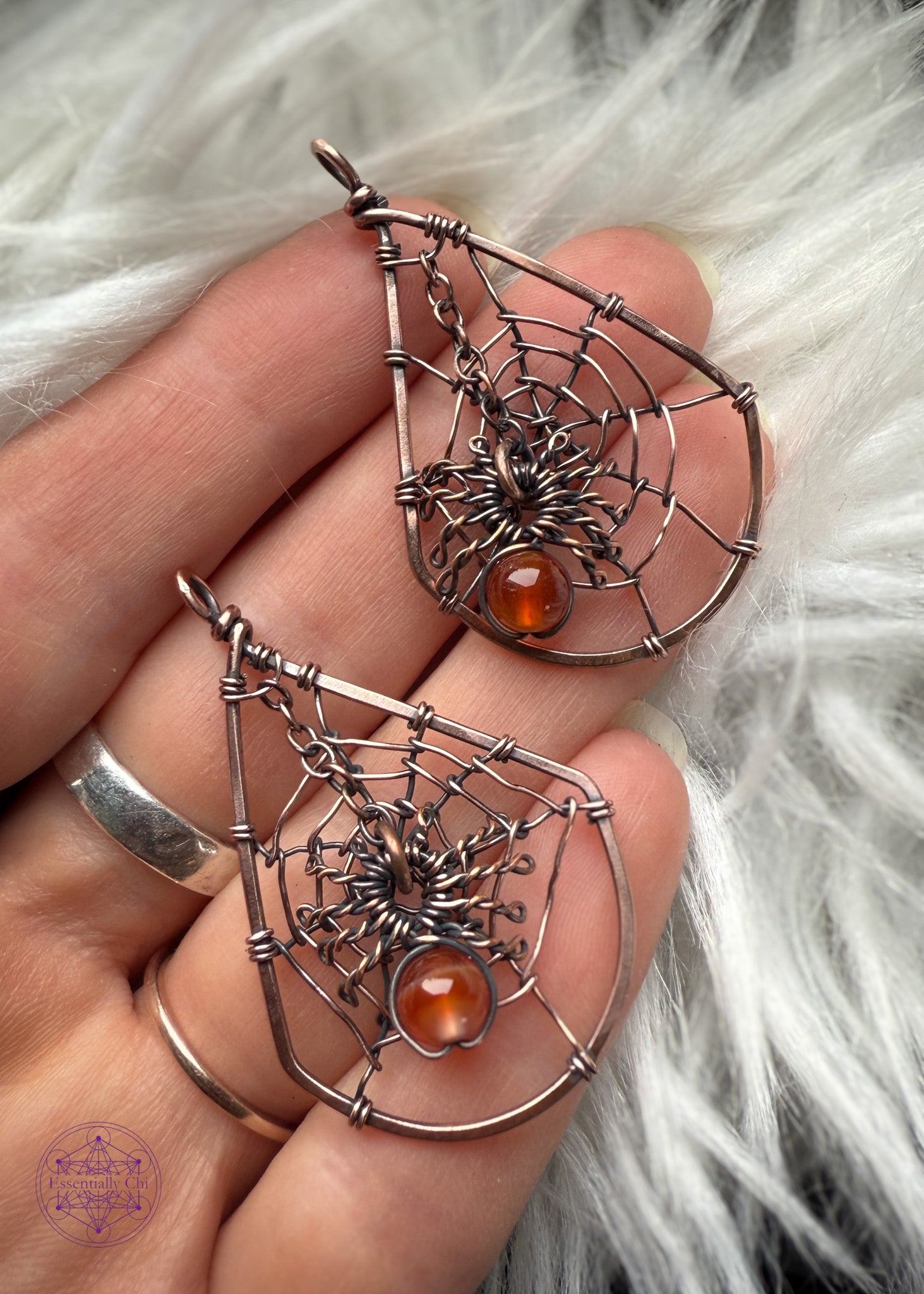 copper wire wrapped spider web earrings held in handover a white faux fur to help the antiqued copper stand out. The web is in a tear drop shape and the spider web dangles from the top over the middle of the web. The spider can have his legs attach to the web if you prefer it not to dangle. Hangs on sterling silver ear hooks.