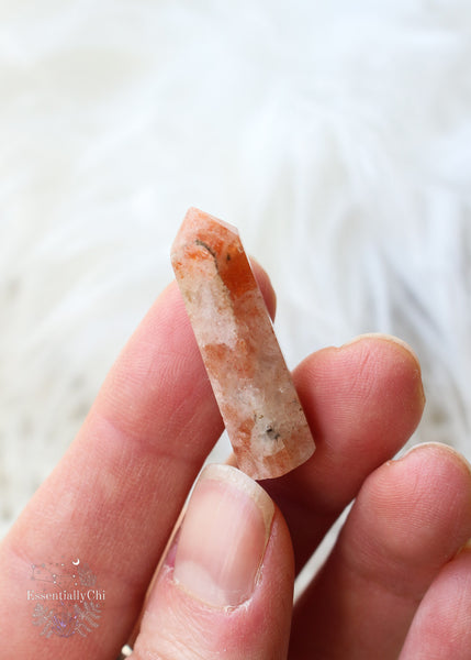 Mini sunstone point about 1" length in hand with variations of light orange with bright orange flash and black spots.