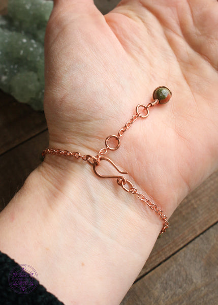 Twisted copper wire wrapped bracelet features Unakite beads. Showing the backside of bracelet on wrist to see hook clasp and beaded extension chain and Unakite charm that you can hold onto to secure the clasp.