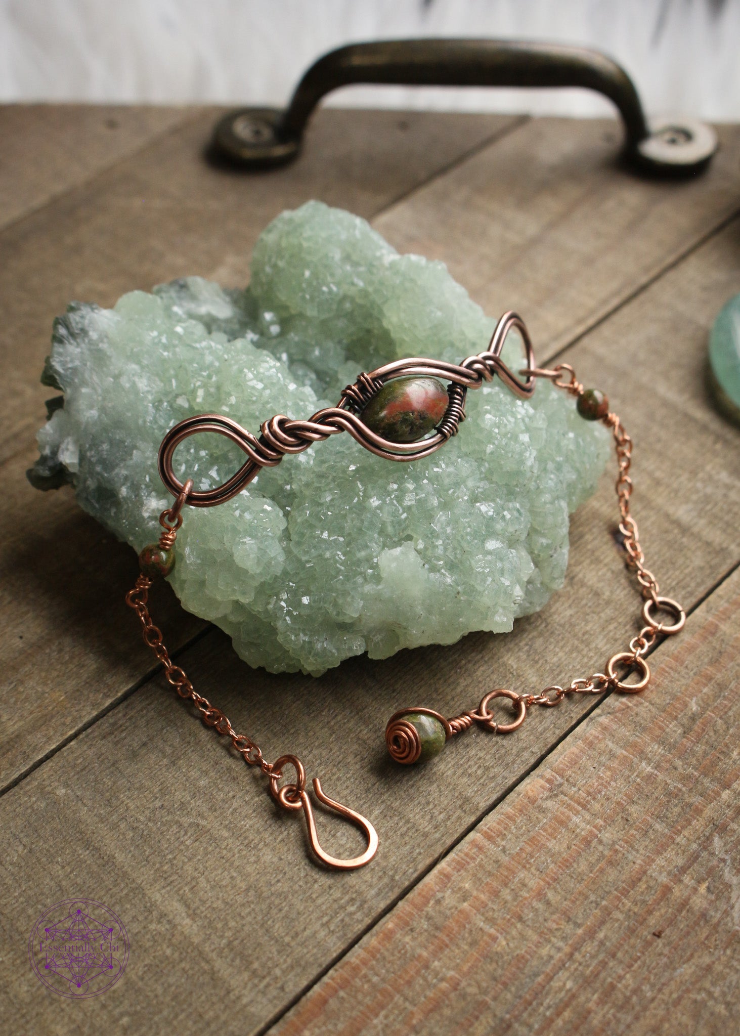 Copper wire wrapped bracelet features an oval Unakite bead wrapped in twisted copper design with loops on each end. Shown on a green crystal to show all the details in the center, sides and clasp. 