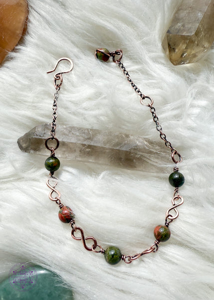 Copper wire wrapped bracelet features 6mm Unakite beads individually wrapped with figure 8 Infinity links in-between for an elegant bracelet. Showing the whole bracelet on a faux white fur blanket to see hook clasp and beaded extension chain and Unakite charm.