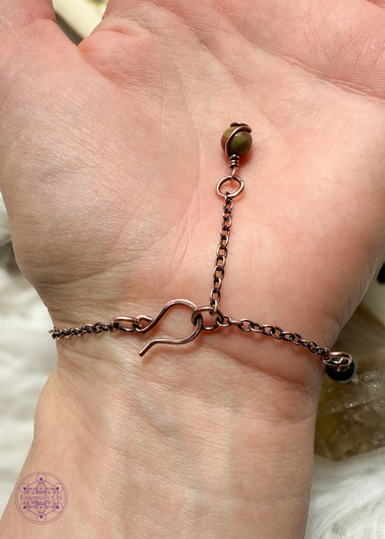 Copper wire wrapped bracelet features 6mm Unakite beads individually wrapped with figure 8 Infinity links in-between for an elegant bracelet. Showing the backside of bracelet on wrist to see hook clasp and beaded extension chain and Unakite charm that you can hold onto to secure the clasp.