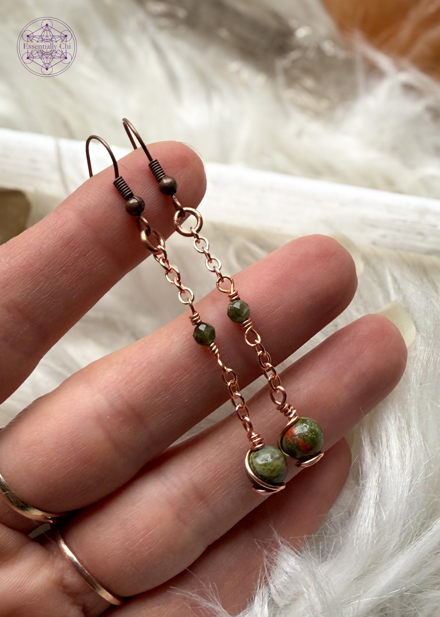 Gorgeous earthy green Unakite dangle earrings hang from a long copper chain and swirled in copper wire with a green tourmaline faceted accent bead hung in the middle of the copper chain. Hung on brass ear hooks gives them a total length of 2.5". Shown in hand for size reference.