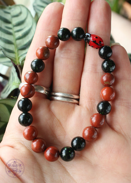 Crystal stretch bracelet with a lampwork glass lady bug focal bead, green goldstone, and red jasper beads. 