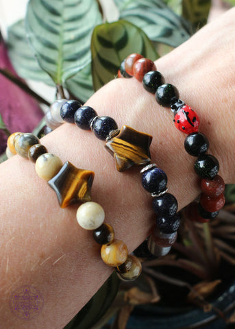 Stack of stretch crystal bracelets, two with a star shaped tiger eye bead, and one with a lampwork ladybug glass bead.