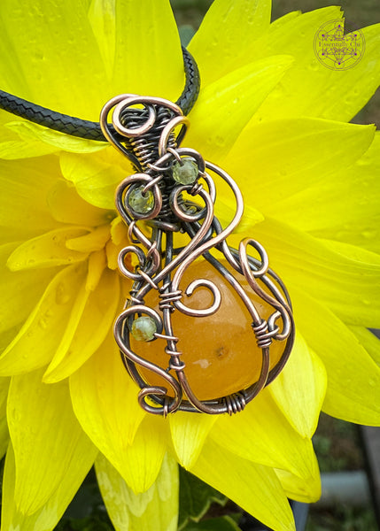 Orange Aventurine mini pumpkin pendant with swirls coming down from the bail and over the front of the pumpkin with three peridot beads in the swirls to act as leaves. Shown on a yellow flower to show off the orange color in the pedant. 