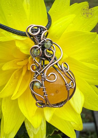Orange Aventurine mini pumpkin pendant with swirls coming down from the bail and over the front of the pumpkin with three peridot beads in the swirls to act as leaves. Shown on a yellow flower to show off the orange color in the pedant. 