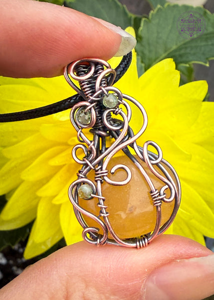 Orange Aventurine mini pumpkin pendant with swirls coming down from the bail and over the front of the pumpkin with three peridot beads in the swirls to act as leaves. Shown in hand for size reference.