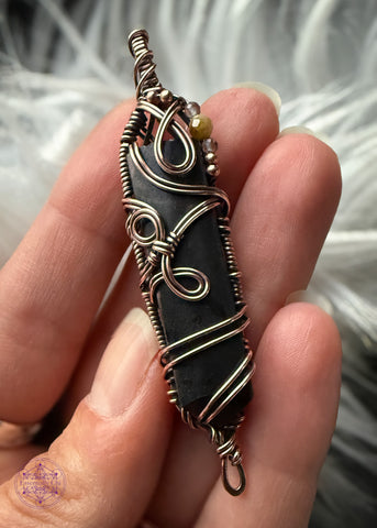 Picture showing a copper wire wrapped pendant in a filagree design around a black tourmaline point and accent beads along the top right of the pendant. Simple thin bail. The copper really makes the black tourmaline really pop out!