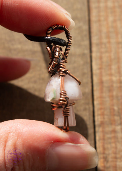 Copper wire wrapped flower agate mushroom pendant with copper swirls along the top and a small cage around the mushroom to keep it stable. The mushroom moves freely like a fidget spinner. Held in hand showing the side details of the pendant.