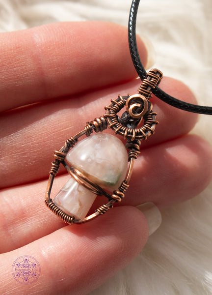 Copper wire wrapped flower agate mushroom pendant with copper swirls along the top and a small cage around the mushroom to keep it stable. The mushroom moves freely like a fidget spinner. Held in hand for size reference in bright light to show details.