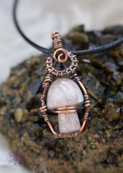 Copper wire wrapped flower agate mushroom pendant with copper swirls along the top and a small cage around the mushroom to keep it stable. The mushroom moves freely like a fidget spinner. Sitting on a Epidote cluster.