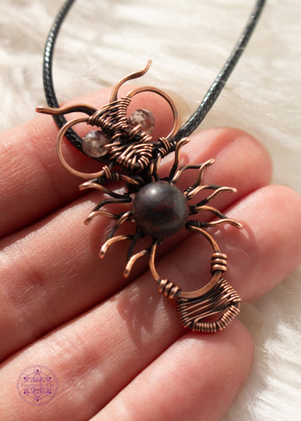 Copper wire wrapped owl pendant with a dark jasper bead for the belly and faceted smoky quartz beads for eyes. held in hand  with a white faux fur background.