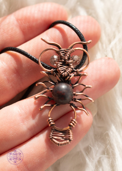 Copper wire wrapped owl pendant with a dark jasper bead for the belly and faceted smoky quartz beads for eyes. held in hand  with a white faux fur background.