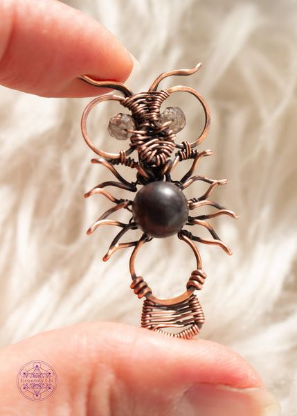 Copper wire wrapped owl pendant with a dark jasper bead for the belly and faceted smoky quartz beads for eyes. held in hand  with a white faux fur background.