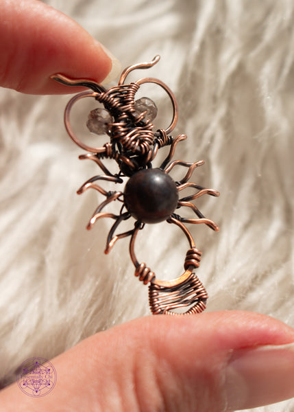 Copper wire wrapped owl pendant with a dark jasper bead for the belly and faceted smoky quartz beads for eyes. held in hand  with a white faux fur background.