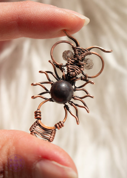Copper wire wrapped owl pendant with a dark jasper bead for the belly and faceted smoky quartz beads for eyes. held in hand  with a white faux fur background.