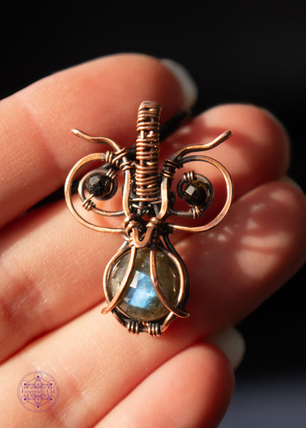 copper wire wrapped pygmy owl pendant with a faceted blue flash labradorite belly and dark green tourmaline beads for eyes, shown held in hand in the light.