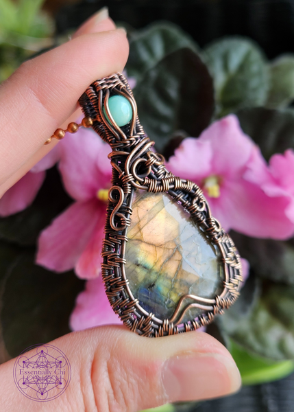 Golden orange and blue flash labradorite in a teardrop shape, with a woven frame and a swirl design on both sides. An aqua green chrysoprase crystal in the bail. 