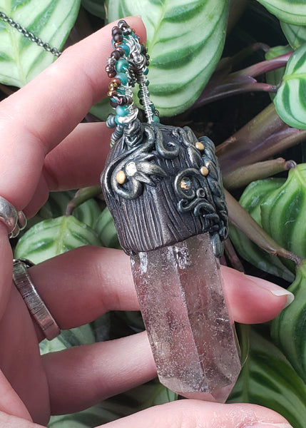Shop the Garden Fairy Pendant. The Garden Fairy aesthetic is to remind you that when life gets tough, to get out in nature and see what Mother Gaia has given you. This beautiful raw smoky quartz point and rutilated tear drop center stone are paired together to help get you thru life's rough patches with ease. Smoky quartz helps transmute negative energy into positive and rutilated quartz helps you dig into shadow work gently and see the good in yourself. The owl stands for wisdom and protection.